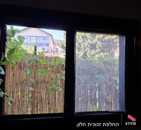 חלון זכוכית במסגרת אלומיניום כהה עם מבט לחצר